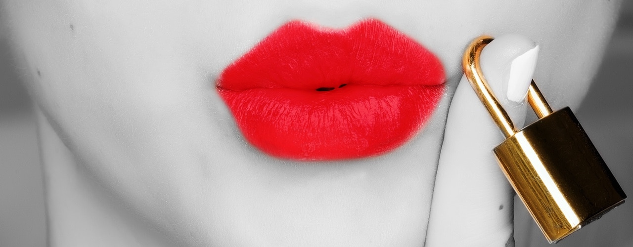 close up image of puckered red lips next to a finger holding a golden lock